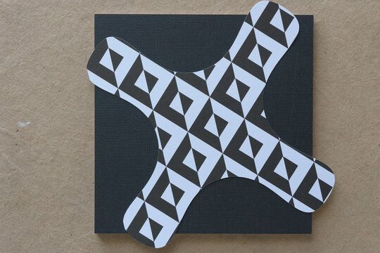 patterned black and white, machine-cut paper tetrad or four lobed shape on a black paper pad and plain brown paper