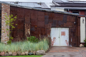 Rusty Corrugated Metal Building With A Peeling White Door Framed By A Brick Corner And Green Grasses