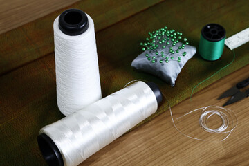 Two spools of white thread lay beside a small pillow with a pin stuck in it. The whole outfit was placed on a wooden table.

