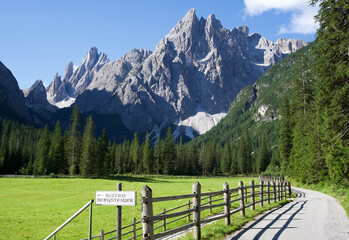 Scenic view of Dolomite mountains with bistro sign and gravel road in lush green valley landscape