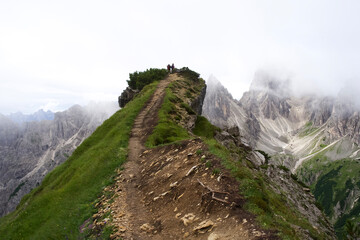 Hikers on a rugged mountain trail surrounded by breathtaking peaks and misty clouds in the Dolomites