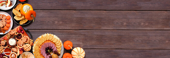 Thanksgiving appetizers, sweets and grazing boards. Overhead view corner border on a dark wood banner background. Pumpkin and apple snacks, pies, turkey cheese platter, desserts.