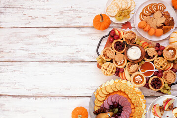 Thanksgiving appetizers, sweets and grazing boards. Above view side border on a white wood background. Pumpkin and apple snacks, pies, turkey cheese platter, desserts.