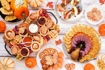 Thanksgiving appetizers, sweets and grazing boards. Above view table scene on a white wood background. Pumpkin and apple snacks, pies, turkey cheese platter, desserts.