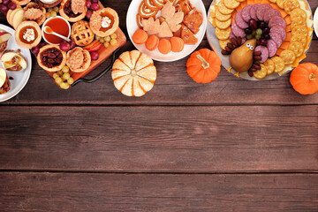 Thanksgiving appetizers, sweets and grazing boards. Overhead view top border on a dark wood background. Pumpkin and apple snacks, pies, turkey cheese platter, desserts.