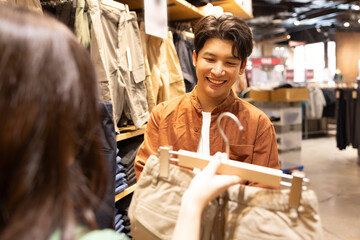 Young Asian couple choosing trousers in a clothing store malls or small shops, Shopping is everyday life concept