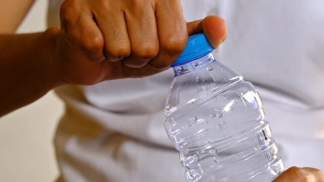 Closeup view 4k stock video footage of 500 ml transparent plastic bottle full of fresh water closed with blue plastic cap isolated on grey wall background. Woman opens bottle