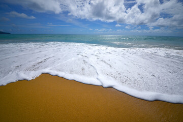 Serene Beachscape: Capturing the moment where the ocean waves gently caress the golden sand under a bright blue sky. This image depicts a moment of peace and tranquility.