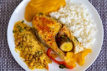 Traditional Brazilian fish moqueca with fresh yellow hake fish fillets, Cynoscion acoupa, with farofa, pirão and white rice. Pescada amarela and dende oil.