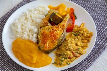 Traditional Brazilian fish moqueca with fresh yellow hake fish fillets, Cynoscion acoupa, with farofa, pirão and white rice. Pescada amarela and dende oil.