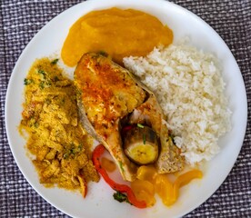 Traditional Brazilian fish moqueca with fresh yellow hake fish fillets, Cynoscion acoupa, with farofa, pirão and white rice. Pescada amarela and dende oil.