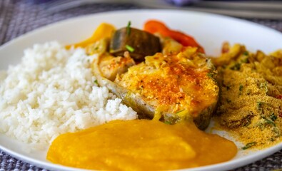 Traditional Brazilian fish moqueca with fresh yellow hake fish fillets, Cynoscion acoupa, with farofa, pirão and white rice. Pescada amarela and dende oil.