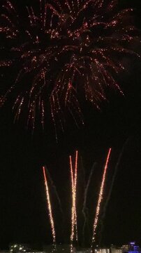 Vertical video. Fireworks on the beach celebrating the end of the fiesta. Multiple powerful charges, flying high and trailing long trails, explode in the sky. Mallorca, Spain.