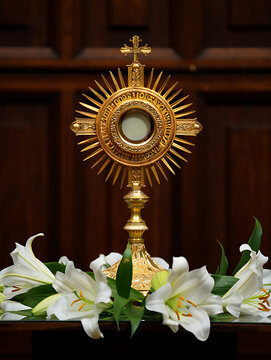 A golden monstrance surrounded by white lilies stands as a symbol of faith and reverence in a serene setting