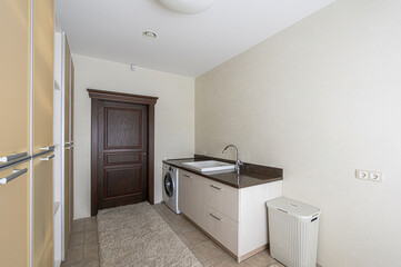 Bright laundry room with a washing machine, sink, counter, and a laundry basket. Neutral color scheme