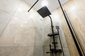A modern shower with beige tiles and a black shower system