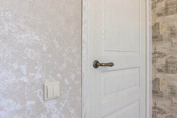 A close-up shows a white door with a handle and a light switch on a textured wall. The wallpaper in the background has images of buildings