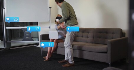 Shaking hands colleagues holding laptop in office lounge, with floating social media icons