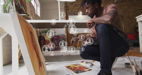 Naklejka premium Crouching artist painting canvas on studio floor, with brush, art supplies and user icons overlay