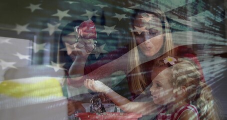 Mother and daughters painting red ornaments with brush, bowls in kitchen with US flag code overlay