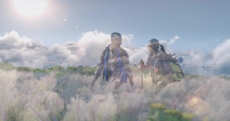 Hiking couple in outdoor gear walking through hillside meadow, with plume grasses and backpacks