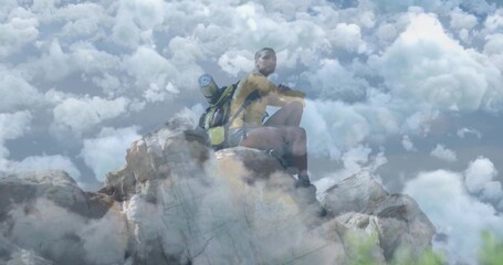 Standing male hiker gazing toward horizon on rocky summit, with backpack and rolled sleeping mat