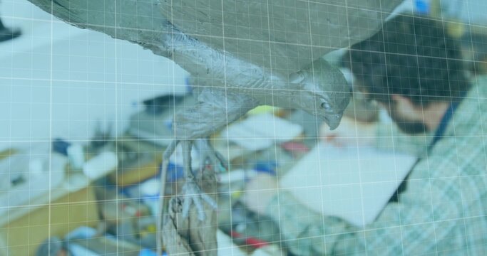Woodworker wearing plaid shirt refining suspended bird sculpture in workshop, with pliers and wires