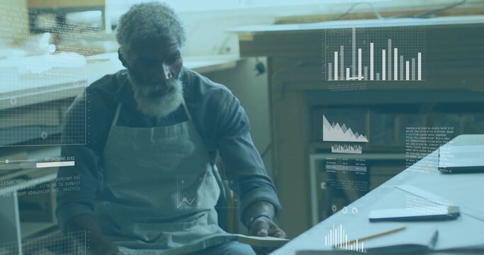 Examining craftsman wearing canvas apron holding wood sample at craft workshop, with digital charts