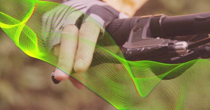 Fototapeta Gripping gloved hand in grey jersey on handlebar lever, forest trail green wave graphic, copy space