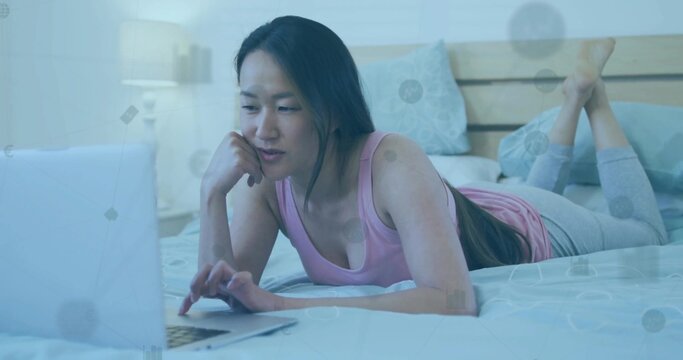 Lying Korean woman in pink top, gray leggings, focusing on laptop in bedroom with network overlay - Powered by Adobe
