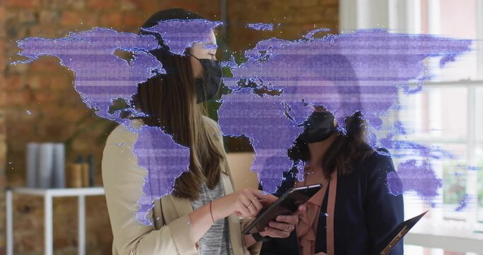 Analyzing world map overlay on tablet by two colleagues in blazers wearing face masks in office