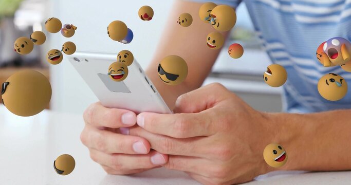 Man wearing striped shirt grasping slim smartphone at white desk, with floating 3D emoji spheres