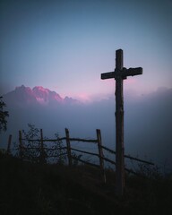 Holzkreuz am Berghang vor Nebel und rosa Berge bei Abendlicht