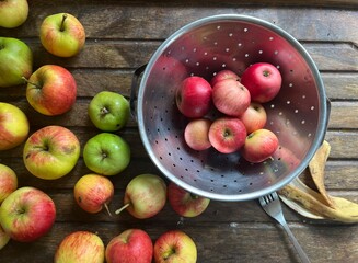 Close up of ripe red and green apples in a colander on a wooden table background the eating and cooking fruit freshly harvest organic allotment orchard garden in Summer interior flat lay view