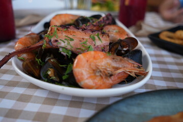 Seafood platter with shrimp, mussels, and octopus served in a restaurant. Fresh Mediterranean cuisine with grilled seafood and herbs on a checkered tablecloth.