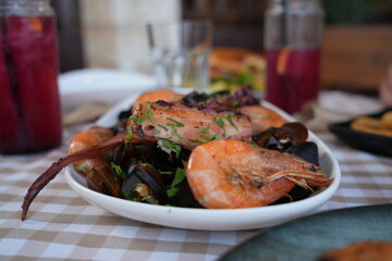 Seafood platter with shrimp, mussels, and octopus served in a restaurant. Fresh Mediterranean cuisine with grilled seafood and herbs on a checkered tablecloth.