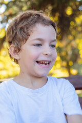 boy in autumn park. A close-up portrait of a happy, smiling boy with curly hair and sparkling blue eyes, sitting on a bench with a warm, autumn-themed background