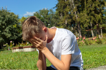 A distressed teenager covers his face with his hands in a park