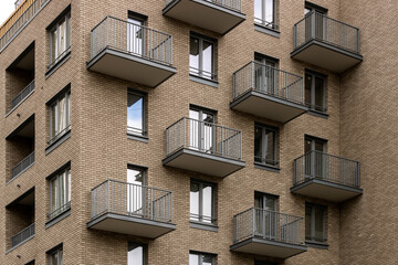 Brick facade of a modern residential building with many identical balconies with metal railings.