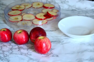 Fresh red apples and sliced apple pieces in a dehydrator on the kitchen table.