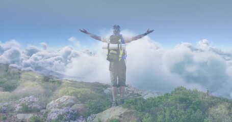 Standing hiker in shorts and boots extending arms toward clouds on mountain ridge with backpack mat