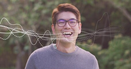 Standing Korean man showing digital waveform overlay in park, wearing eyeglasses and grey sweater