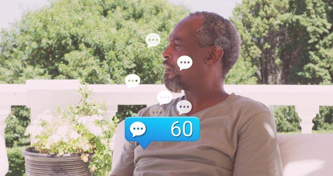 Relaxing senior man wearing tee on porch sofa surrounded by floating 60 chat bubbles, copy space - Powered by Adobe