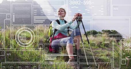 Pausing woman hiker in hiking boots holding trekking poles on grassy hillside, with green backpack