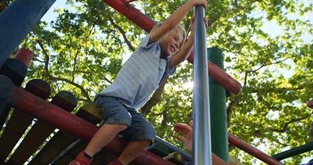 Climbing child wearing striped t-shirt, shorts grabbing silver pole at park under adult hand