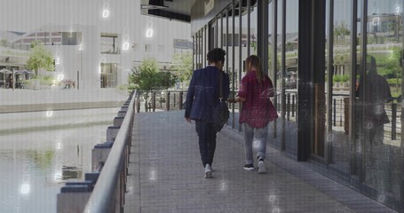 Two business casual colleagues walking waterfront walk with black shoulder bag and canal railing