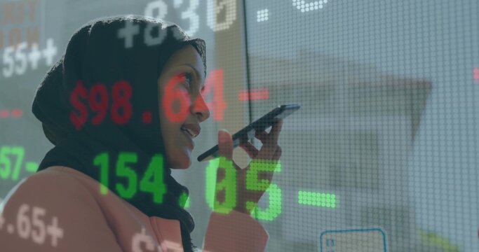 Executive wearing black hijab blazer speaking into smartphone in office by glass with data overlay
