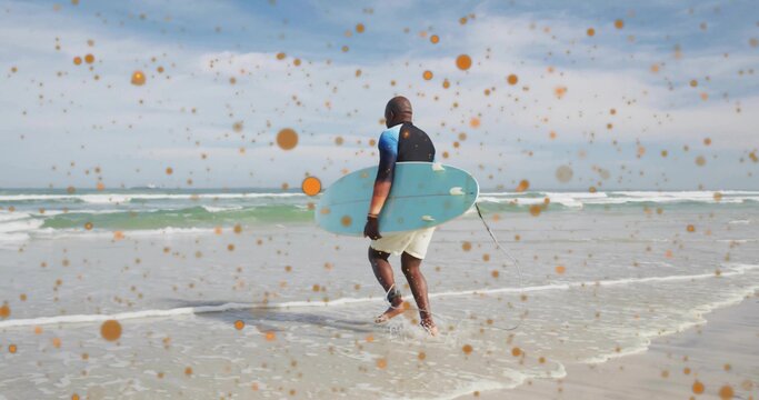 Walking senior surfer carrying blue surfboard into shallow shoreline with leash and orange spots