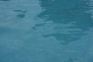 Blue swimming pool water surface with gentle ripples and sunlight reflections. Calm aqua texture creating a refreshing and relaxing summer atmosphere. Perfect background for vacation, spa, and wellnes
