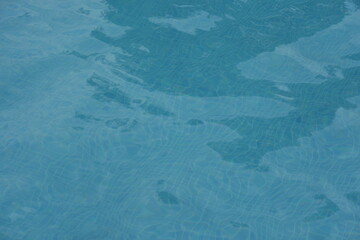 Blue swimming pool water surface with gentle ripples and sunlight reflections. Calm aqua texture creating a refreshing and relaxing summer atmosphere. Perfect background for vacation, spa, and wellnes